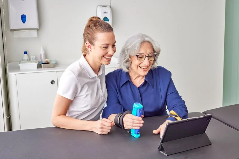 An older adult squeezing the GripAble sensor while a staff member holds the tablet