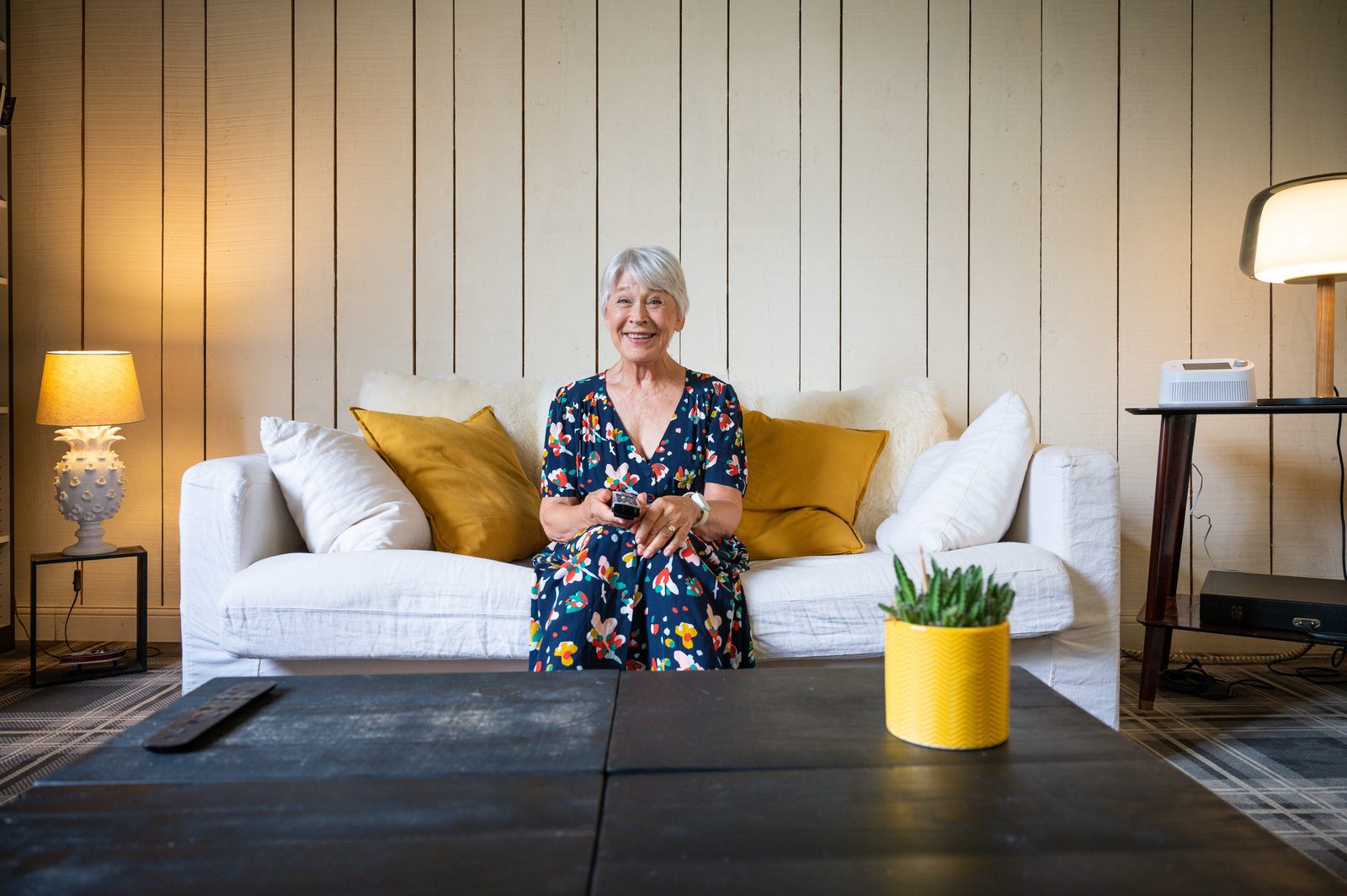 An older woman sitting in her living room with the Vibby Hub on a side table behind her
