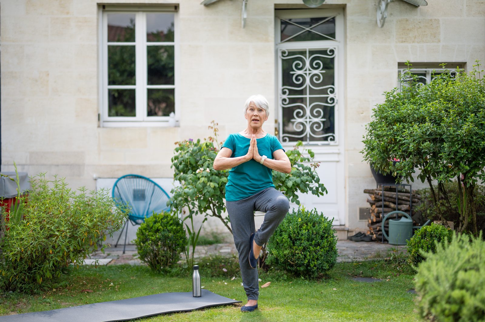 An older woman doing a balance pose in her garden, wearing the Vibby Oak on her wrist